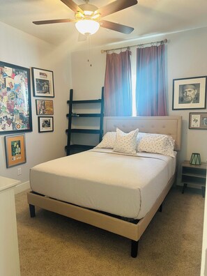 A bedroom with a bed, a ceiling fan, a window with curtains, and various framed pictures on the walls. - Bertram Tranquility- 3 Bedroom 2 Bath Hideaway (Bertram)