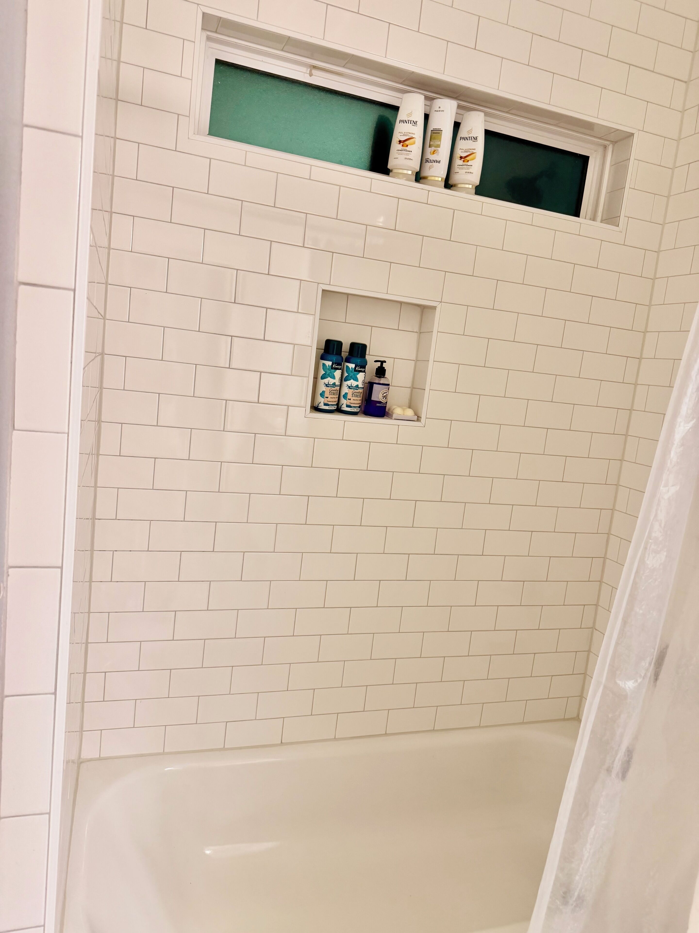 Ein Badezimmer mit weiß gefliesten Wänden, einer Badewanne und Regalen für Toilettenartikel.