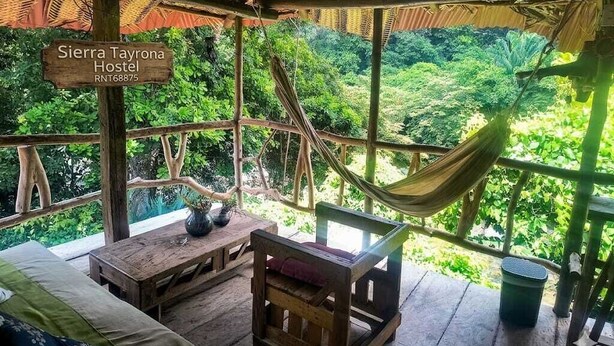 Une structure rustique en bois, dotée d’un hamac, d’un canapé et d’une table, qui offre une vue sur un paysage verdoyant et luxuriant.
