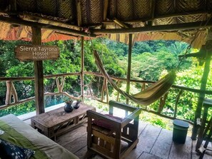 Une structure rustique en bois, dotée d’un hamac, d’un canapé et d’une table, qui offre une vue sur un paysage verdoyant et luxuriant.