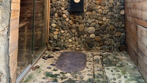 Un espace douche aux murs en pierre, agrémenté d’un panneau vertical noir et de plusieurs pommeaux de douche circulaires.