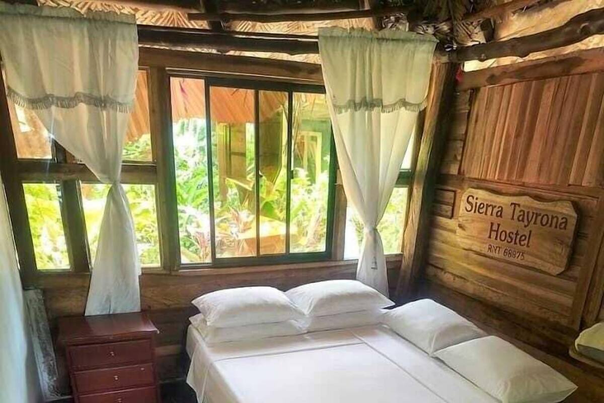 A wooden room with a bed, a nightstand, a dresser, and a sign reading 'Sierra Tayrona Hostel.'