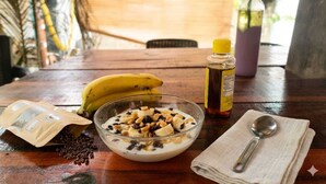 Une table en bois sur laquelle se trouvent un bol de céréales, une banane, une bouteille de sirop et une cuillère posée sur une serviette.