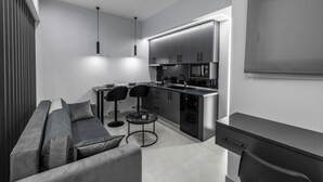 A modern kitchen with a central island, two bar stools, and a sofa. - Kamara Urban Retreat by #db Premium Stay Apartments  (Thessaloniki)