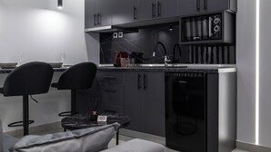 A modern kitchen with dark cabinetry, a built-in microwave, and a compact refrigerator. - Kamara Urban Retreat by #db Premium Stay Apartments  (Thessaloniki)