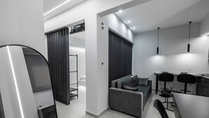 A modern living space with a grey sofa, a dining area with two chairs, and a kitchen with a dining table. - Kamara Urban Retreat by #db Premium Stay Apartments  (Thessaloniki)