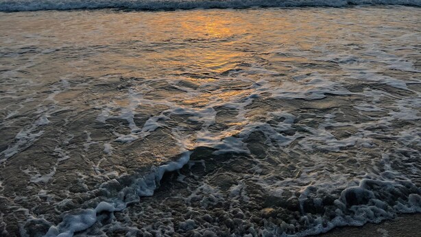 Une plage au coucher du soleil, où les vagues viennent doucement lécher le rivage.