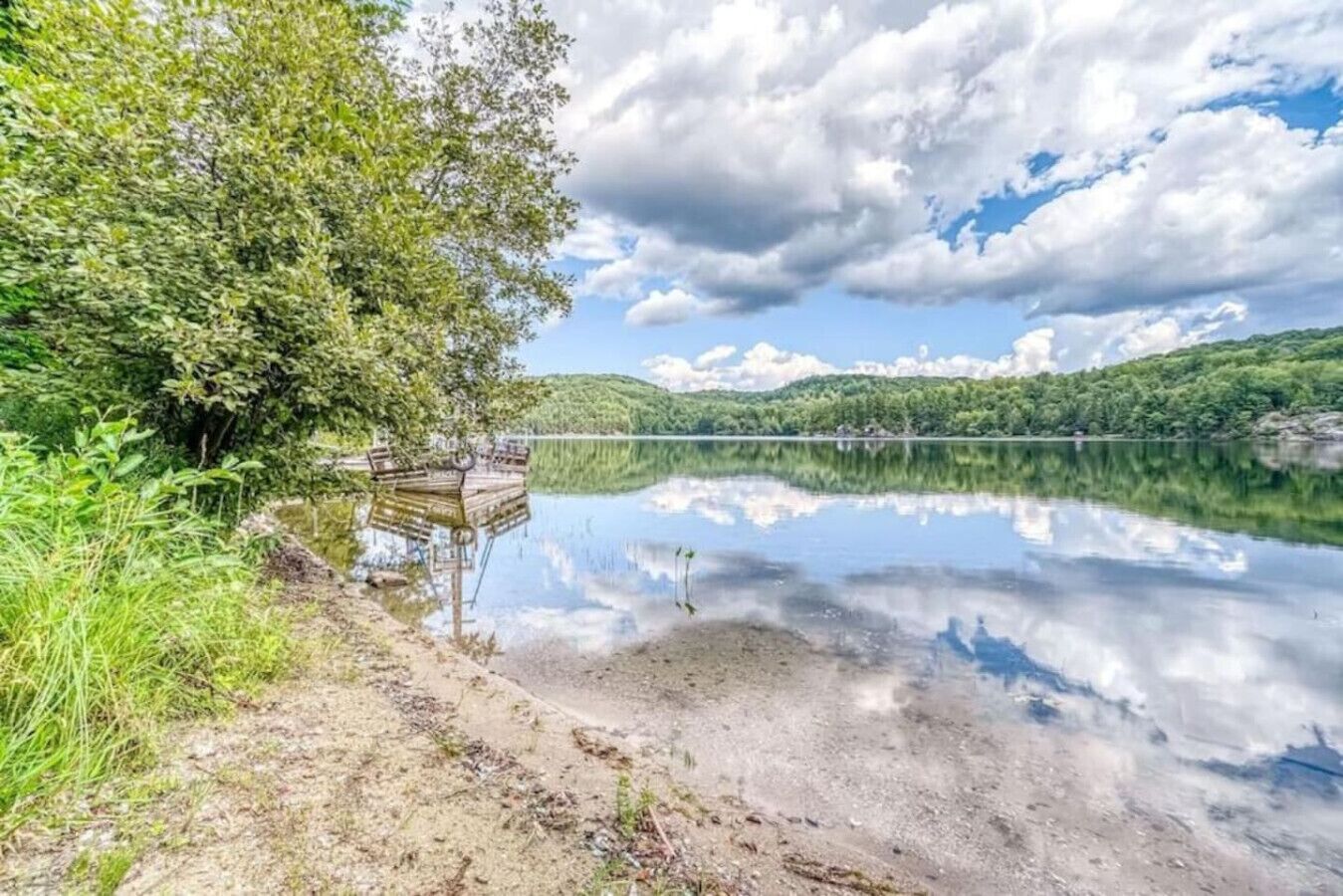 A tranquil lake with a dock, surrounded by lush greenery and a clear sky.