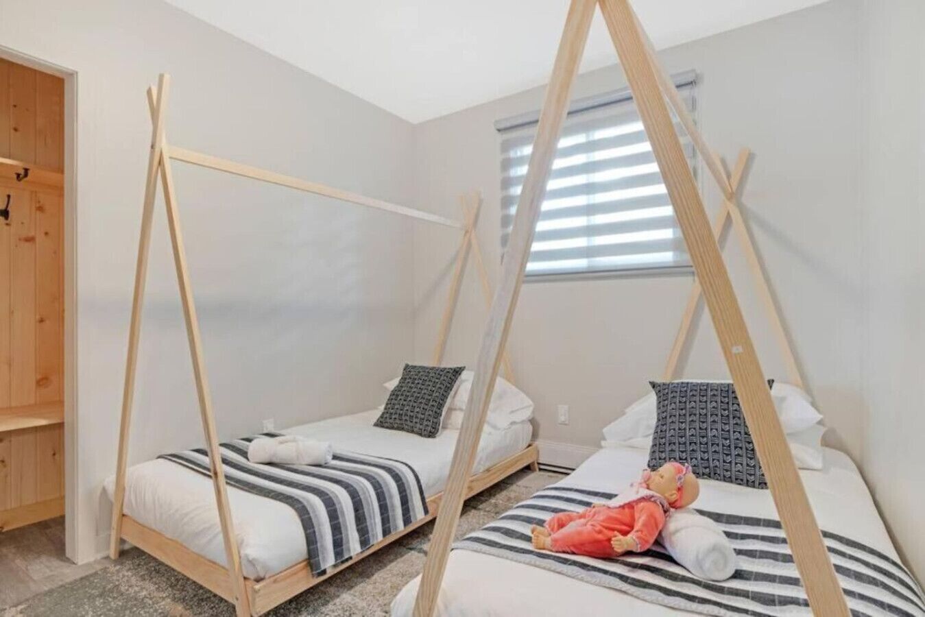 A bedroom with two wooden bunk beds, a window with blinds, and a wooden wardrobe.