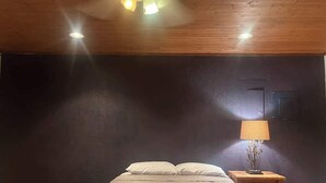 Een slaapkamer met een bed, een nachtkastje met een lamp en een donkere muur.