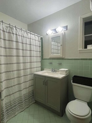 A bathroom with a striped shower curtain, a sink with a mirror above it, and a toilet. - Sleepy Hollow Villa (Rosenberg)