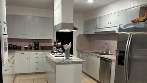 Een moderne keuken met witte kastjes, een centraal eiland, roestvrijstalen apparatuur en een betegelde vloer.
