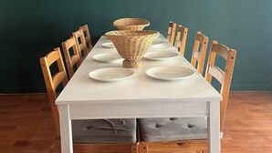 Een eettafel met witte borden en een gevlochten mand, omringd door houten stoelen.