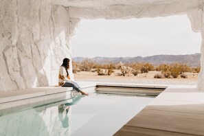 A person sitting by a pool with a desert landscape in the background. - La Cave ~The Cave Pool House + Spa  (Joshua Tree)