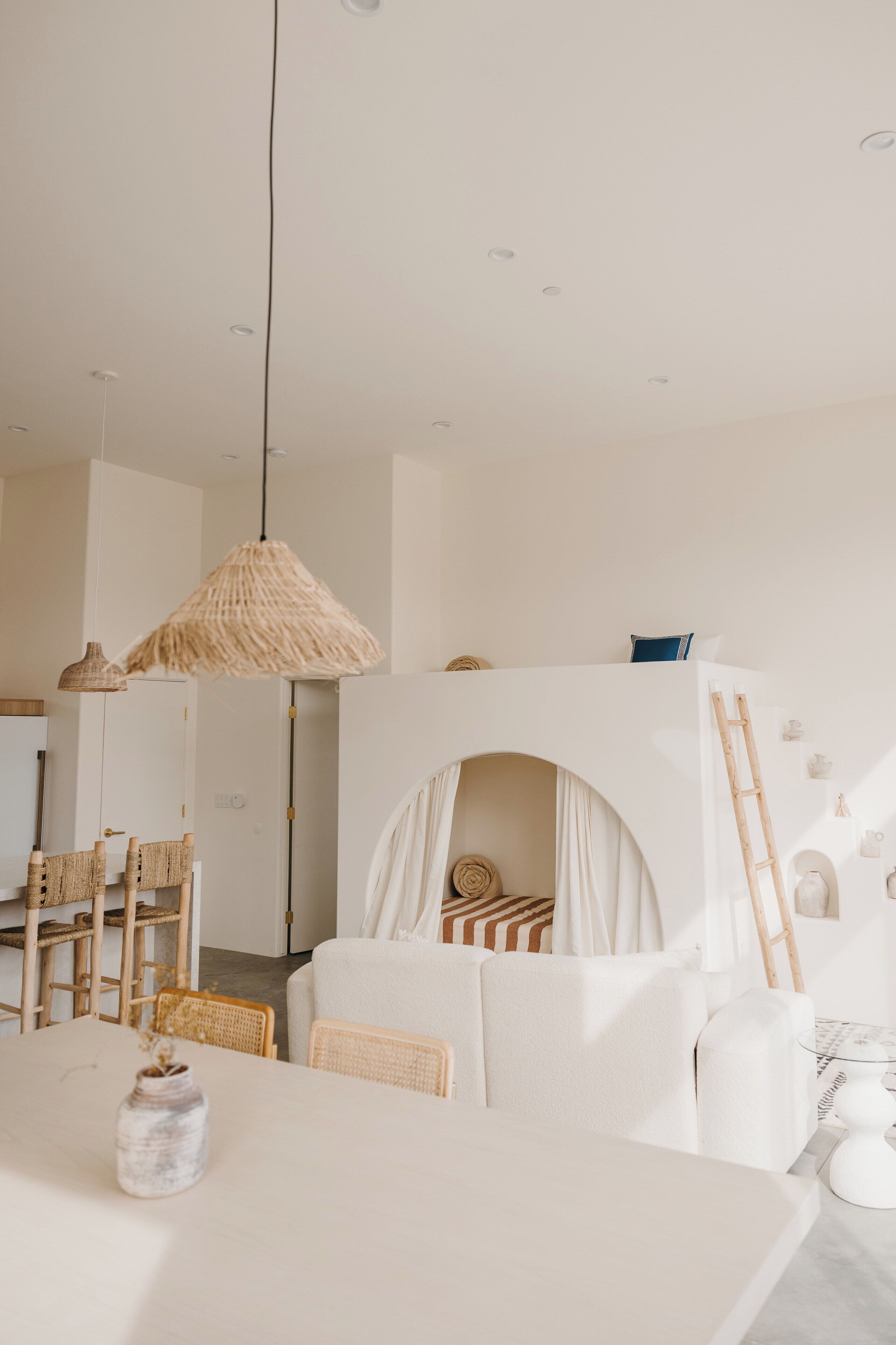 A modern, minimalist room with a bunk bed, a dining table, wicker furniture, and a hanging light fixture.