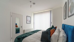 A bedroom with a bed, a window with blinds, a door, and a wall-mounted light fixture.