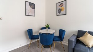 A modern dining area with a round table, blue upholstered chairs, and two framed artworks on the wall.