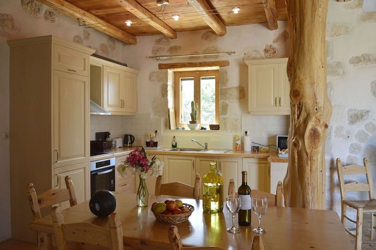 A rustic kitchen with stone walls, wooden beams, and a large window.