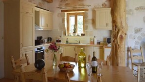 A rustic kitchen with stone walls, wooden beams, and a large window. - Villa Ariadne - Stylish vacation home with all amenities (Melidoni)