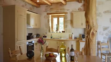 A rustic kitchen with stone walls, wooden beams, and a large window.