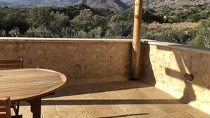 A patio with a round wooden table and chairs, a stone wall, and a view of mountains. - Villa Ariadne - Stylish vacation home with all amenities (Melidoni)