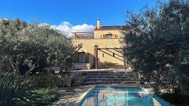 A stone building with a pool, surrounded by olive trees and a clear blue sky. - Villa Ariadne - Stylish vacation home with all amenities (Melidoni)
