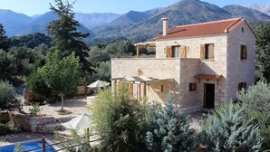A stone house with a red-tiled roof, a pool, and a mountainous backdrop. - Villa Ariadne - Stylish vacation home with all amenities (Melidoni)