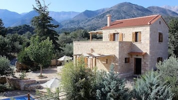 A stone house with a red-tiled roof, a pool, and a mountainous backdrop.