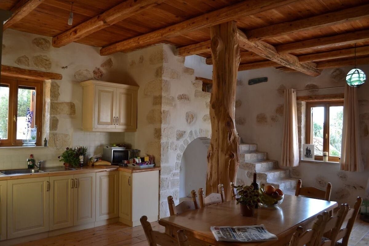A rustic kitchen with stone walls, wooden beams, and a dining table with chairs.