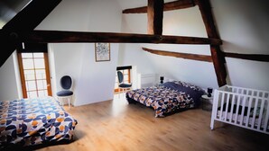 A bedroom with two beds, a chair, and a crib.