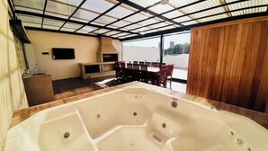 Un espace détente avec un jacuzzi, des chaises en bois et un téléviseur mural.