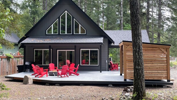 Eine moderne Holzhütte mit einer Terrasse, roten Stühlen und einer kleinen Holzkonstruktion.
