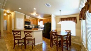 A modern kitchen with wooden cabinets, a central island with bar stools, and a dining area with a table and chairs.