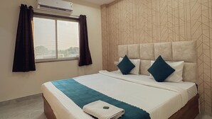 A modern hotel room with a large bed, a ceiling fan, an air conditioning unit, and a window with curtains. - Hotel Atharv Inn (Indore)