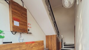 A reception area with a wooden reception desk, a wall-mounted sign, a ceiling fan, and a staircase leading to an upper level. - Hotel Atharv Inn (Indore)