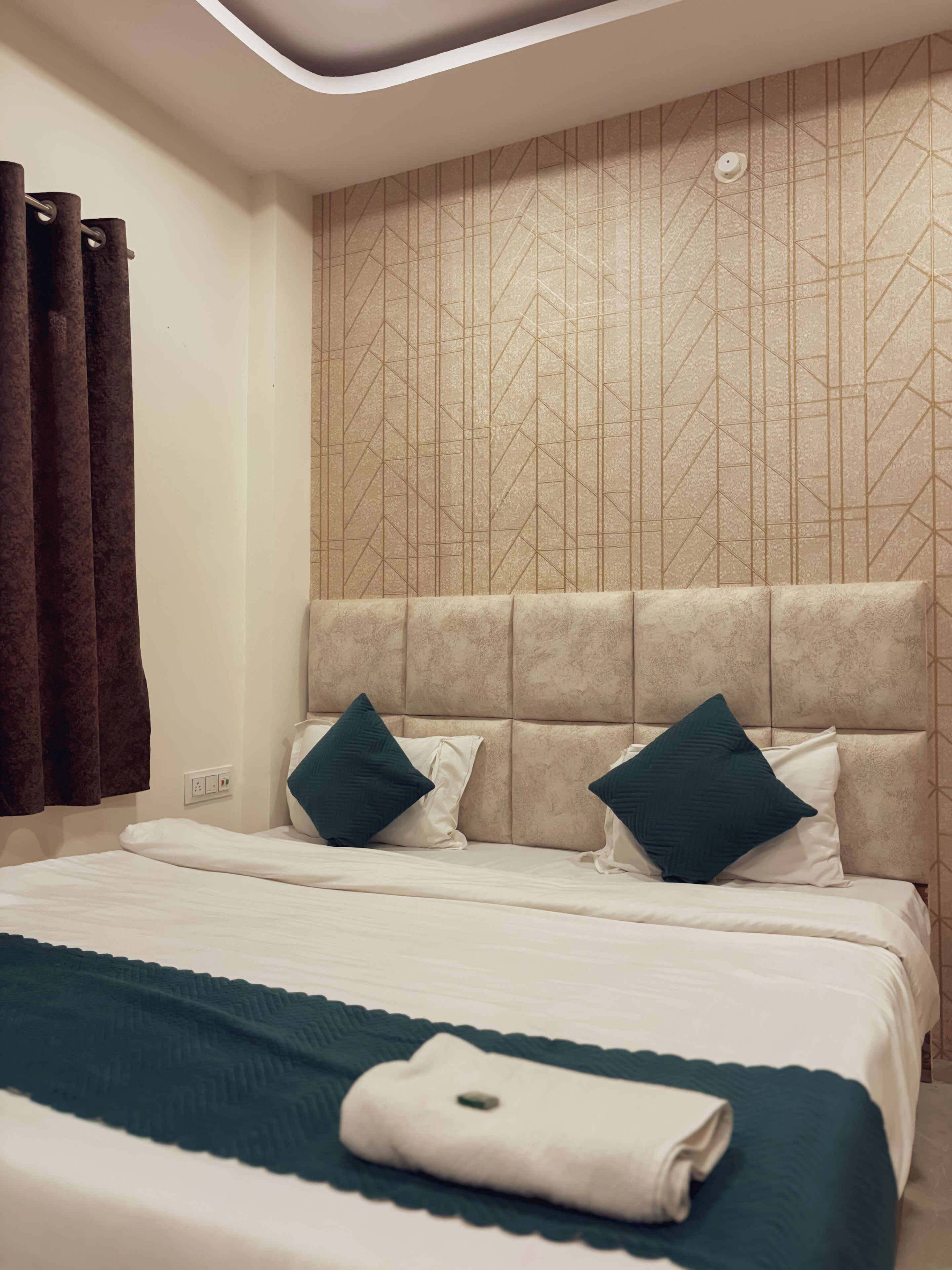 A modern hotel room with a large bed, two pillows, a headboard, and a patterned wall.