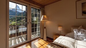 A bedroom with a large sliding glass door leading to a balcony, a bed with white bedding, a lamp, and a framed picture on the wall. - Chalet Les Ecureuils (Zermatt)