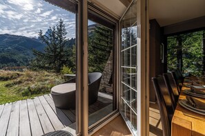 A modern outdoor dining area with a wooden deck, a glass door leading to a scenic mountain view, and a set table with chairs. - Chalet Les Ecureuils (Zermatt)