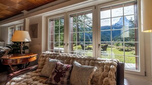 A cozy room with a fur-covered sofa, a table with a lamp, and large windows offering a mountain view. - Chalet Les Ecureuils (Zermatt)