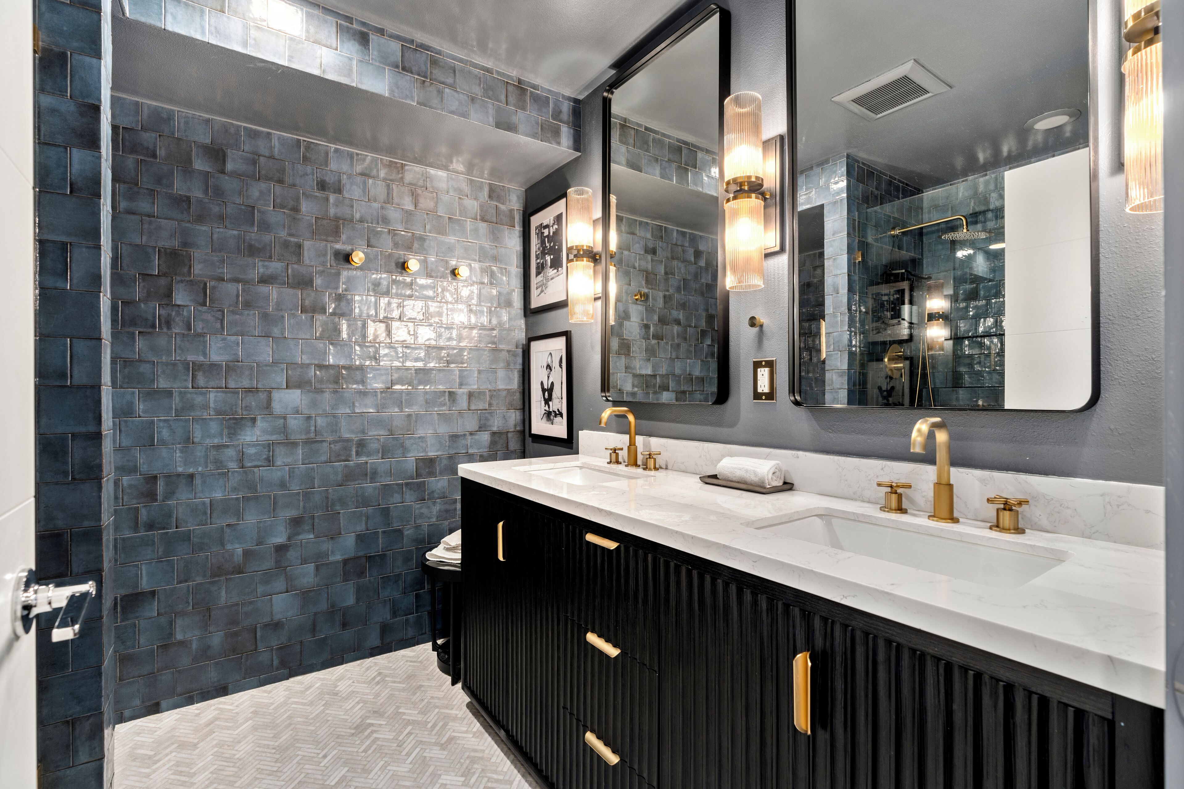 A modern bathroom with a large mirror, two sinks, and a black vanity with gold handles.