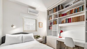 Un dormitorio con cama, mesita de noche, lámpara y una amplia estantería.