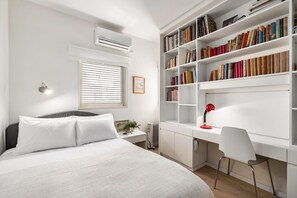 A bedroom with a bed, bedside table, lamp, and a large bookshelf.