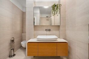 A modern bathroom with a large mirror, a white sink, and a toilet.