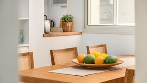 A dining table with a fruit bowl, wicker chairs, and a window with a view of buildings.