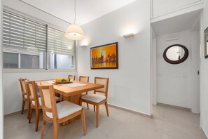 A dining area with a wooden table and chairs, a painting on the wall, and a round mirror.