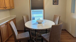 A dining area with a round table, four wicker chairs, a white tablecloth, a glass bowl, and a pendant light. - Spacious Peaceful 2-bedroom home in Saint Ignatius, Montana with amazing views. (Saint Ignatius)