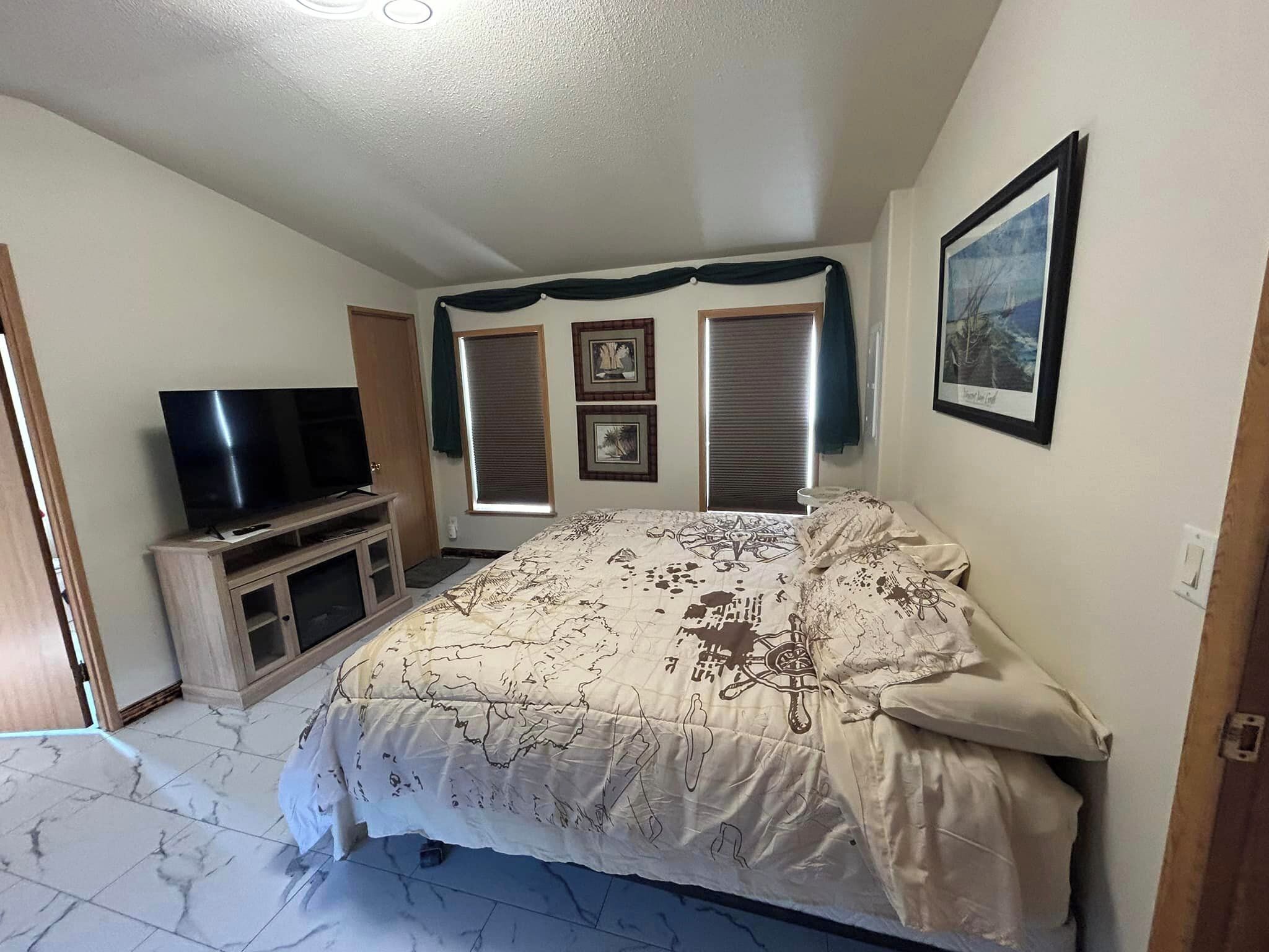 A bedroom with a bed, a TV, and a window with blinds.