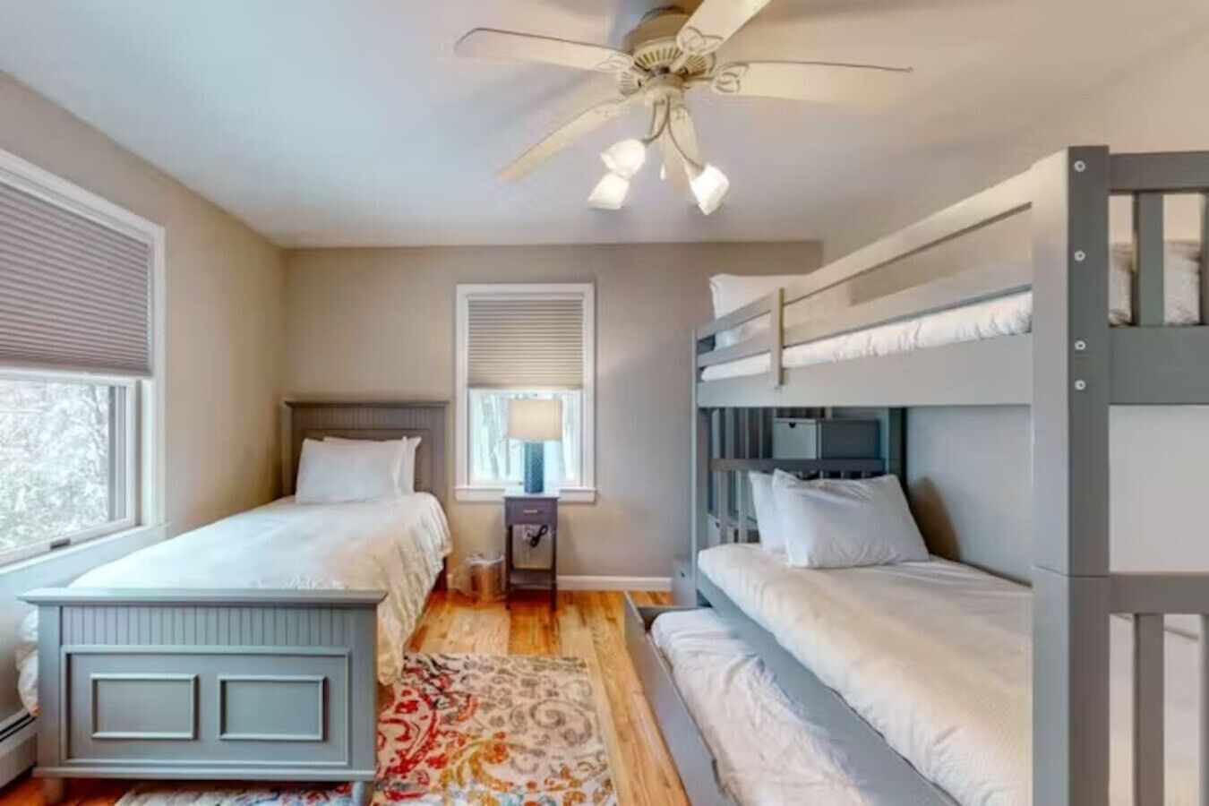 Ein Schlafzimmer mit Etagenbetten, Deckenventilator, Nachttisch mit Lampe und Fenster mit Jalousien.