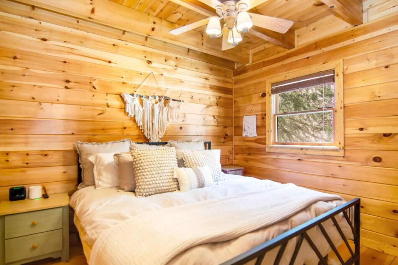 A wooden cabin bedroom with a bed, nightstand, and a ceiling fan.