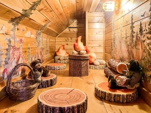 Una stanza accogliente con pareti e soffitto in legno, decorata con quadri di animali e animali di pezza. Sono presenti degli sgabelli rotondi in legno e un cesto di vimini.